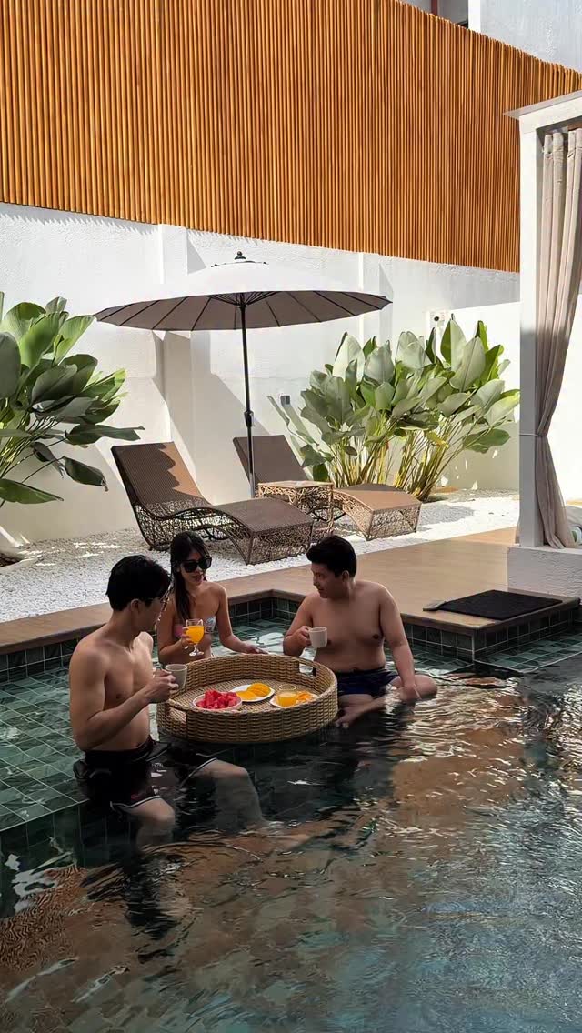 Three guests in the pool with a floating fruit tray — rattan loungers and bamboo fence in background