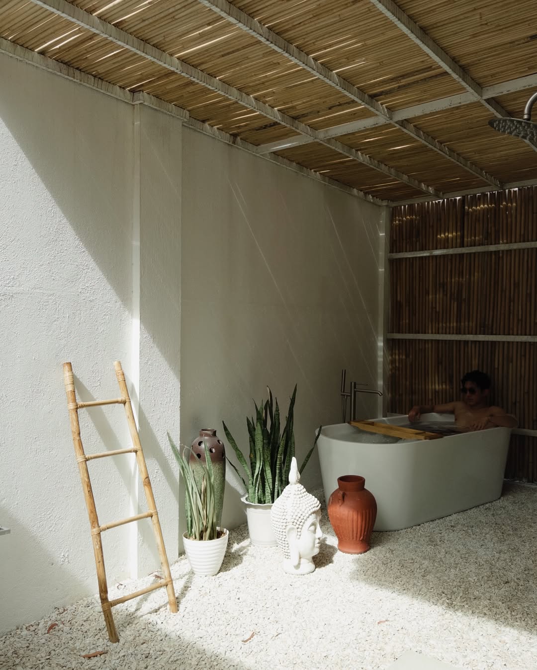Open-air bathroom with bamboo ceiling, freestanding tub, and tropical plants